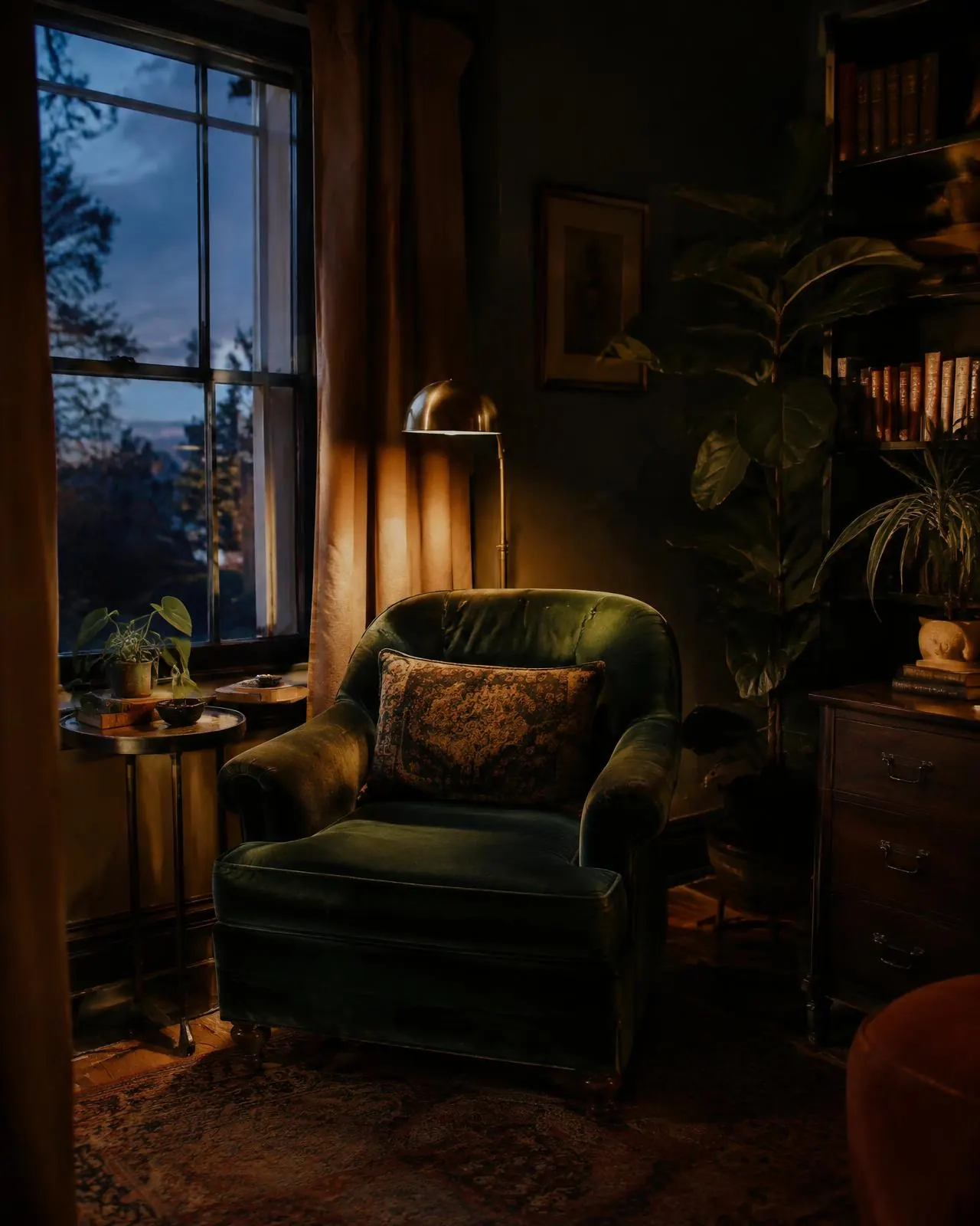 A velvet armchair beside the window, lamp glowing
